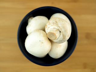 White mushrooms in black bowl on wooden board