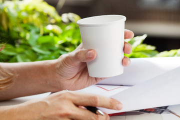 Disposable coffee cup in hand. Woman drinking coffee at work 