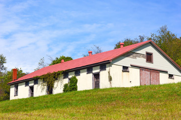 Fototapeta na wymiar Stables built on a grassy hill under a blue sky with clouds.