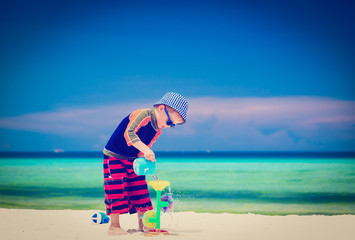 Fototapeta na wymiar little boy playing with water on sand beach