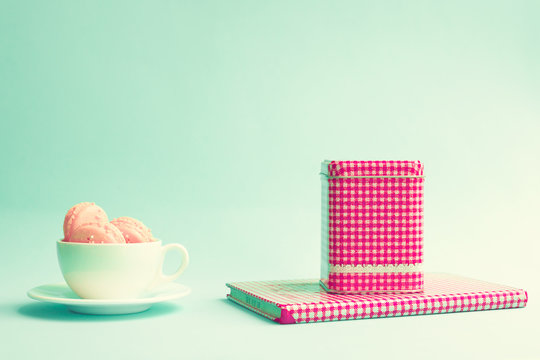 Pink macaroons in a white tea cup and tea tin over book