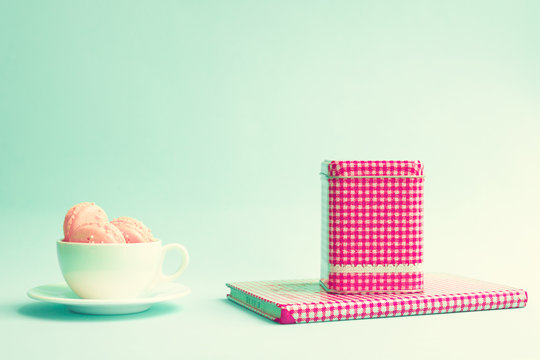 Pink macaroons in a white tea cup and tea tin over book