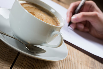 Person writing a letter with cup of coffee