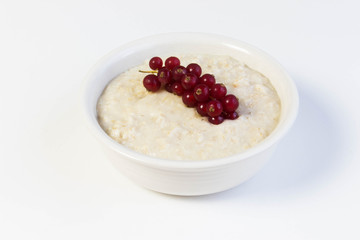 Bowl of oats porridge with red currant  on a white background