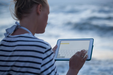 Woman typing on tablet PC by sea