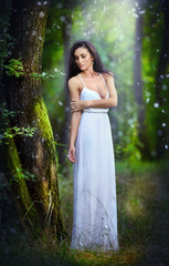 Lovely young lady wearing an elegant long white dress in forest