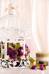 Spa candle in front of white bird cage filled with flowers.