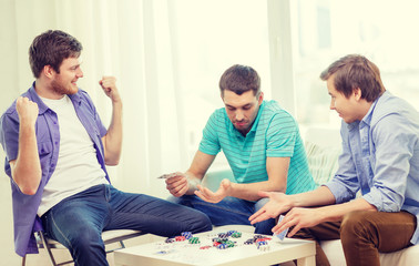 Fototapeta premium happy three male friends playing poker at home