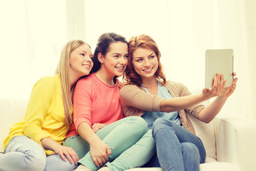 three smiling teenage girls with tablet pc at home