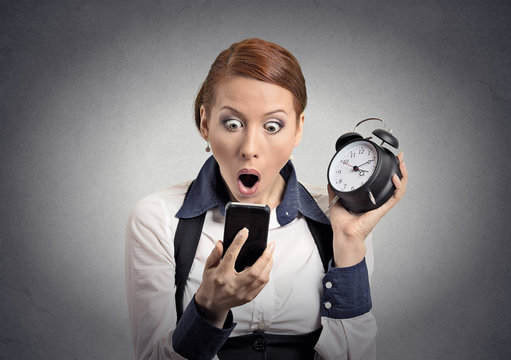 shocked business woman with alarm clock looking at phone
