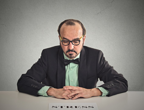 Sad stressed man sitting at office desk on grey wall background 