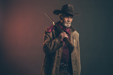 Old rough western cowboy with gray beard and brown hat holding r