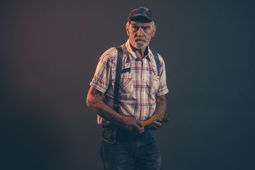 Senior carpenter with gray hair and beard holding yellow measuri