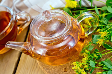Herbal tea from tutsan in glass teapot with cup on board