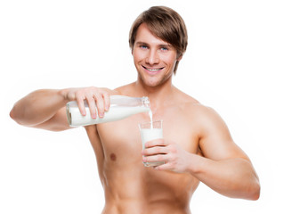 Young  muscular man pouring milk into a glass .