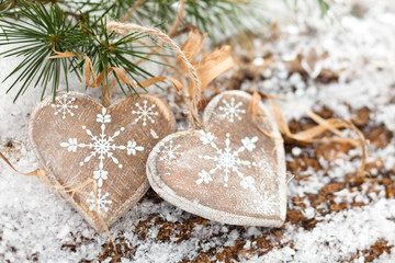 Wooden hearts on snow-covered wooden background.
