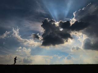 Obraz na płótnie Canvas Lonesome jogger Dramatic sky with jogger running - backlighting