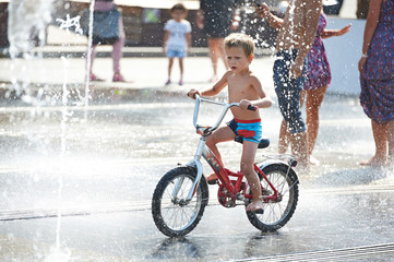 Little boy rides his bike among fountains
