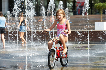 Little girl rides his bike among fountains