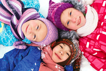 children lie on the snow in winter and look upwards