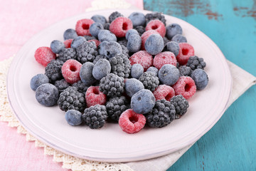 Iced berries on plate, on color wooden background