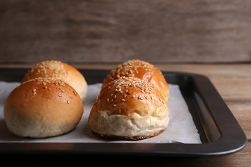 Tasty buns with sesame on oven-tray, on wooden background