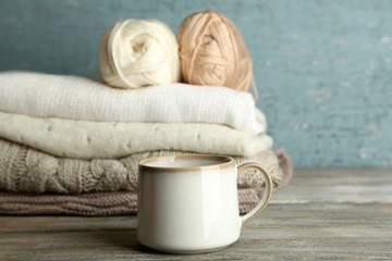 Cup of hot drink, knitting clothes and yarn on wooden