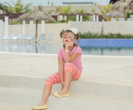 Little unhappy girl with painted face sitting near the pool