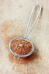 Cocoa powder in silver sieve on a rustic wooden board