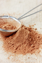 Cocoa powder in silver sieve on a rustic wooden board