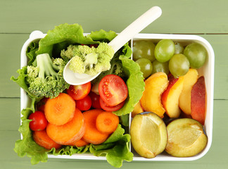 Tasty vegetarian food in plastic box on green wooden table