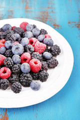 Iced berries on plate, on color wooden background