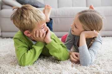 Cute silblings smiling at each other on rug