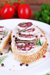 Sandwiches with salami on plate on napkin on wooden background