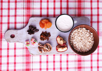 Bowl of oatmeal, mug of yogurt, marmalade, chocolate, raisins,