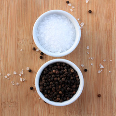 Coarse salt and black peppercorns in white ceramic bowls