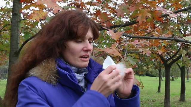 Woman blowing his nose at autumn park. Outdoor.