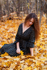 Young girl sitting on leafs in autumn park