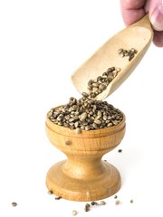 Hemp seeds poured from a wooden spoon in to a bowl white