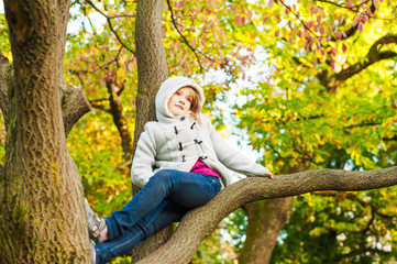 Autumn portrait of a cute little girl playing on a tree