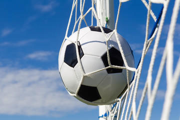 Soccer football in Goal net with sky field.