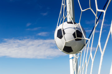 Soccer football in Goal net with sky field.