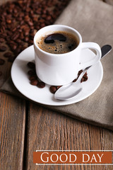 Cup of coffee and coffee beans on napkin on wooden background