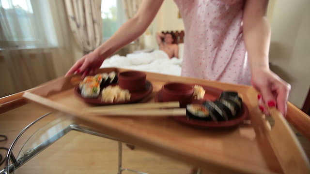 Wife bringing tray with Japanese sushi to husband in bed