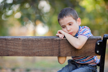 orphan, unhappy boy sitting on a park bench and crying