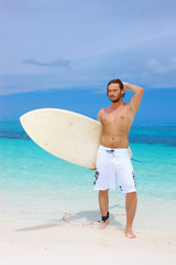 Naklejka na ściany i meble Handsome surfer posing with his surfboard