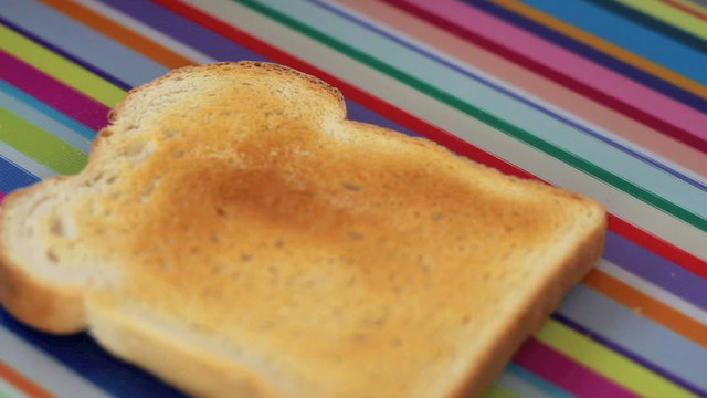 Close up toast being buttered against colorful background.