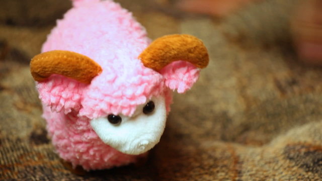 woman's hand playing toy pink sheep on couch closeup