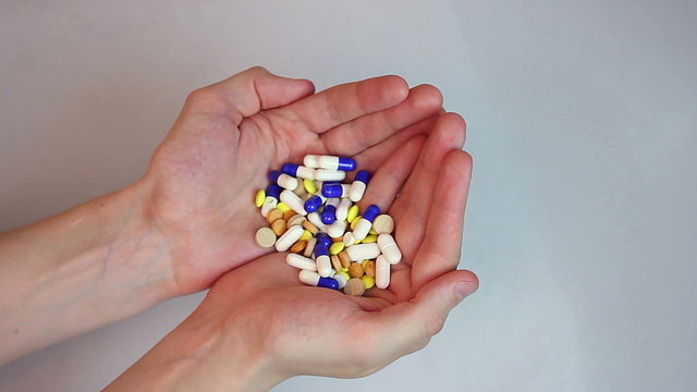 Person holding two handfuls of colorful tablets and capsules
