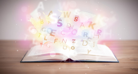 Open book with glowing letters on concrete background